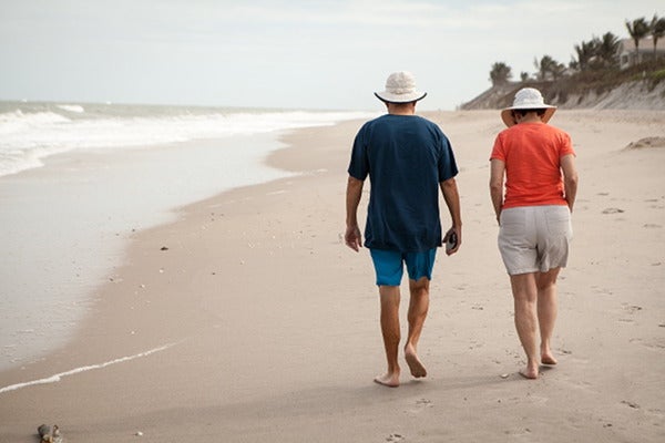 職場探しのことを相談しながら浜辺を歩くシニア夫婦